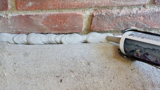 Caulking the gap with concrete caulk and caulk gun between home foundation and concrete slab
