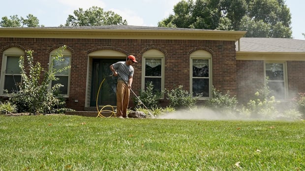Man using spray nozzle pressure washer on walkway in front of home