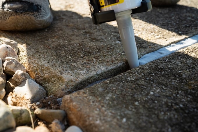 Applying concrete caulk to expansion joint between two sidewalk slabs