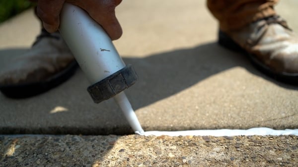 Caulk gun laying concrete caulk in expansion joint on concrete sidewalk