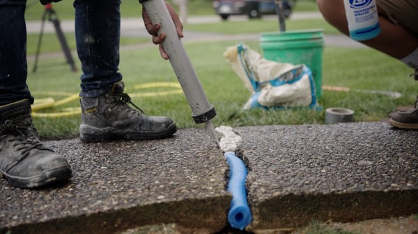 Concrete repair technician caulking a large crack between two concrete sidewalk slabs