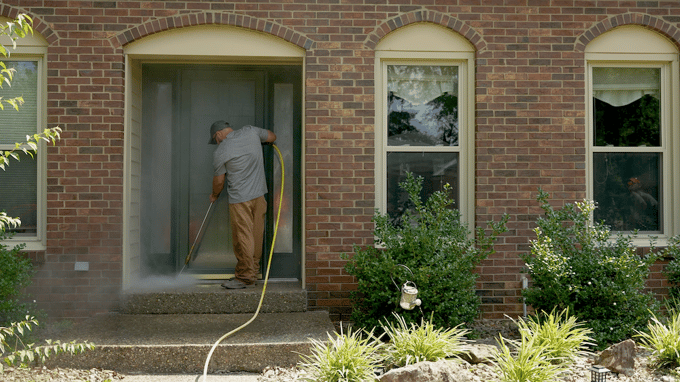 Man cleaning front porch of home with wand pressure washer attachment