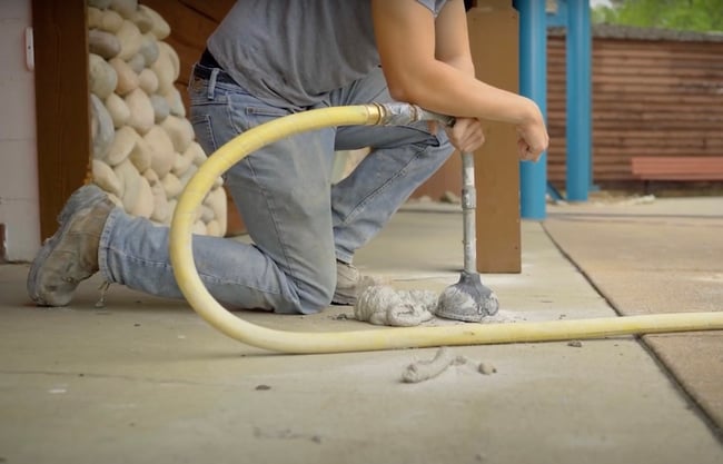 Man injecting stone slurry grout concrete leveling solution beneath sunken concrete in order to lift it back up in commercial setting