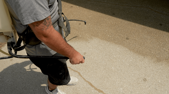 Man spraying penetrating concrete sealer onto clean concrete driveway