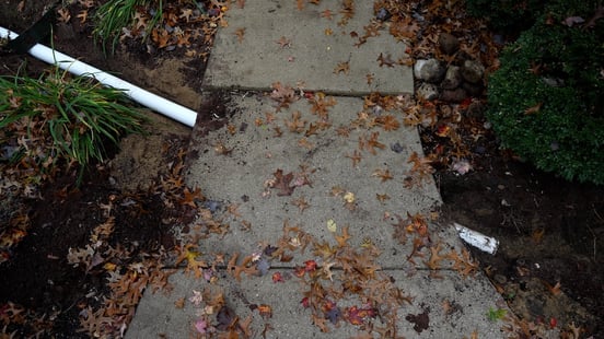 Downspout drainage pipe buried under the sidewalk