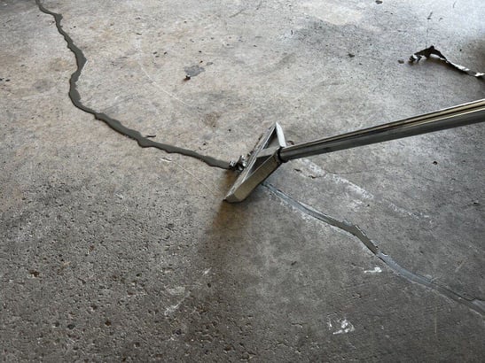 Polyurea crack filler being scraped off the surface of garage floor