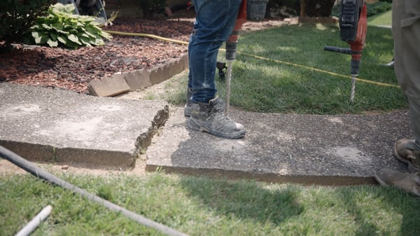 Concrete repair technicians working on fixing large crack and trip hazard on concrete sidewalk