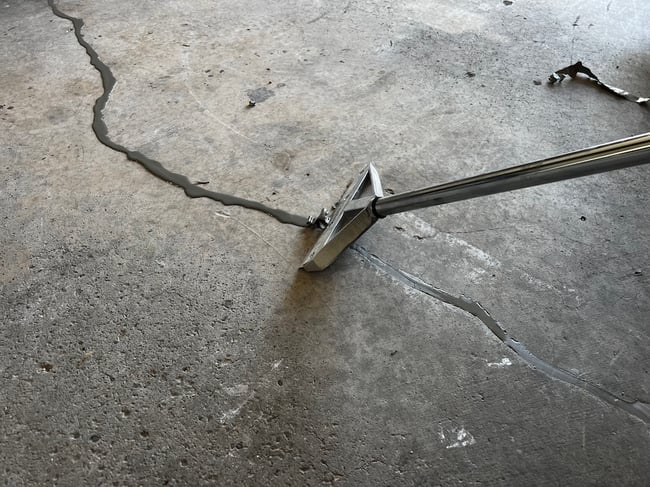 Polyurea crack filler applied to crack in garage floor being scraped smooth with metal tool