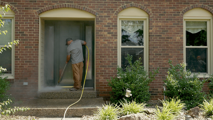 Man pressure washing front porch of a brick home