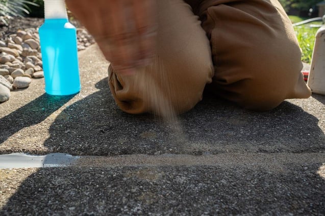 Hand sprinkling sand on concrete caulk to blend in adjoining slabs