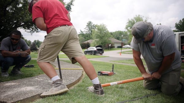 Concrete repair technicians using pry bars to shift a concrete slab back into place